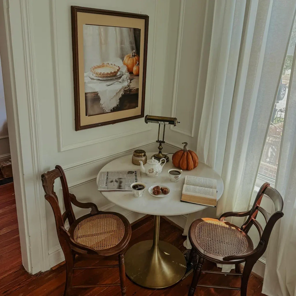 A single velvet pumpkin, a small brass lidded jar, a teapot, and a lamp. Everything else on the surface is a cup, a plate, or something being read.